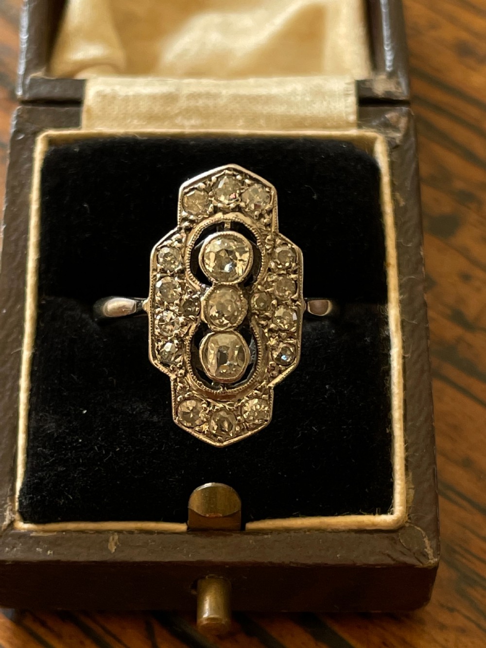 An Edwardian platinum and diamond panel ring featuring three central round diamonds within an elongated geometric frame. View III