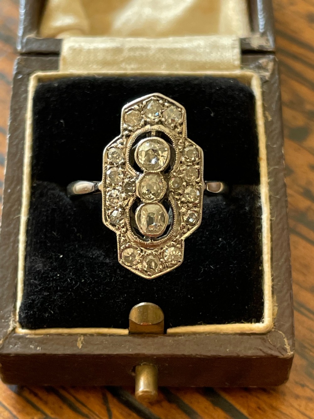 An Edwardian platinum and diamond panel ring featuring three central round diamonds within an elongated geometric frame. View IV