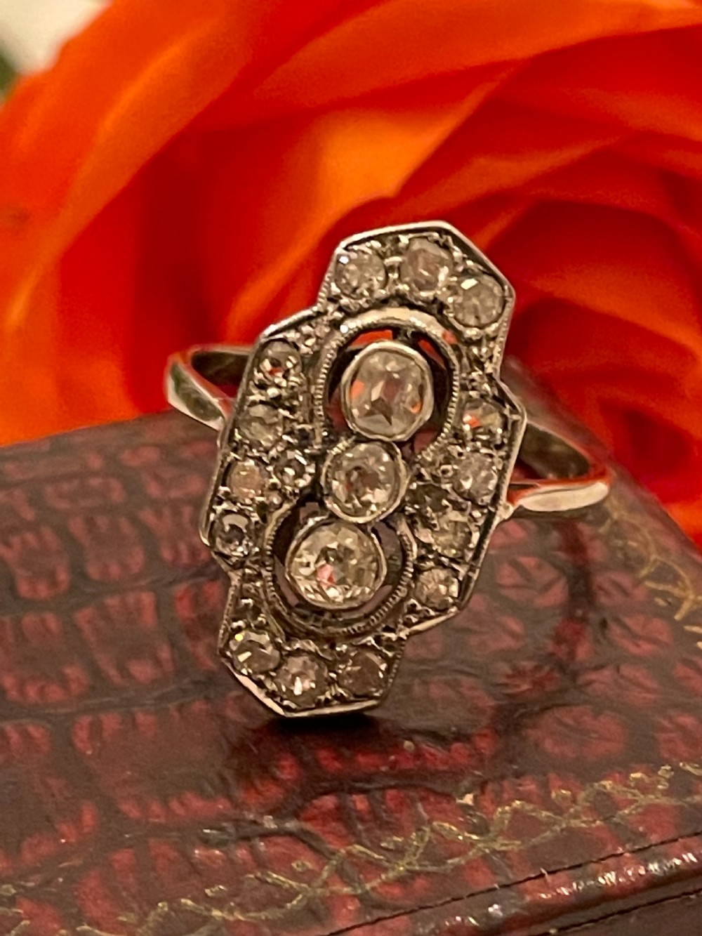 An Edwardian platinum and diamond panel ring featuring three central round diamonds within an elongated geometric frame. View V