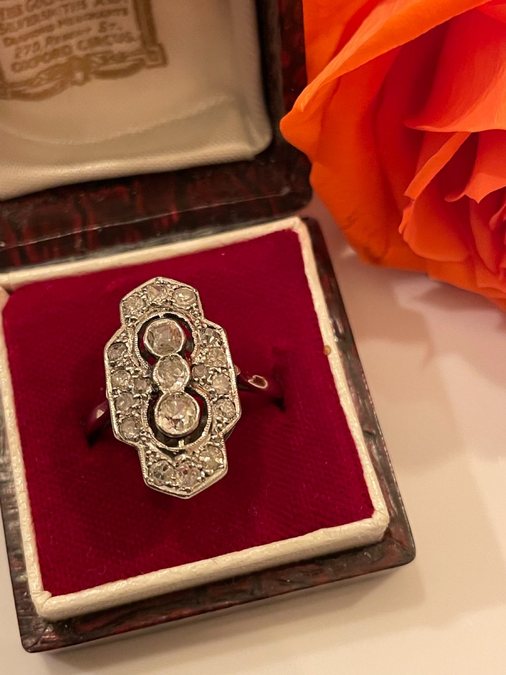 An Edwardian platinum and diamond panel ring featuring three central round diamonds within an elongated geometric frame. View VI
