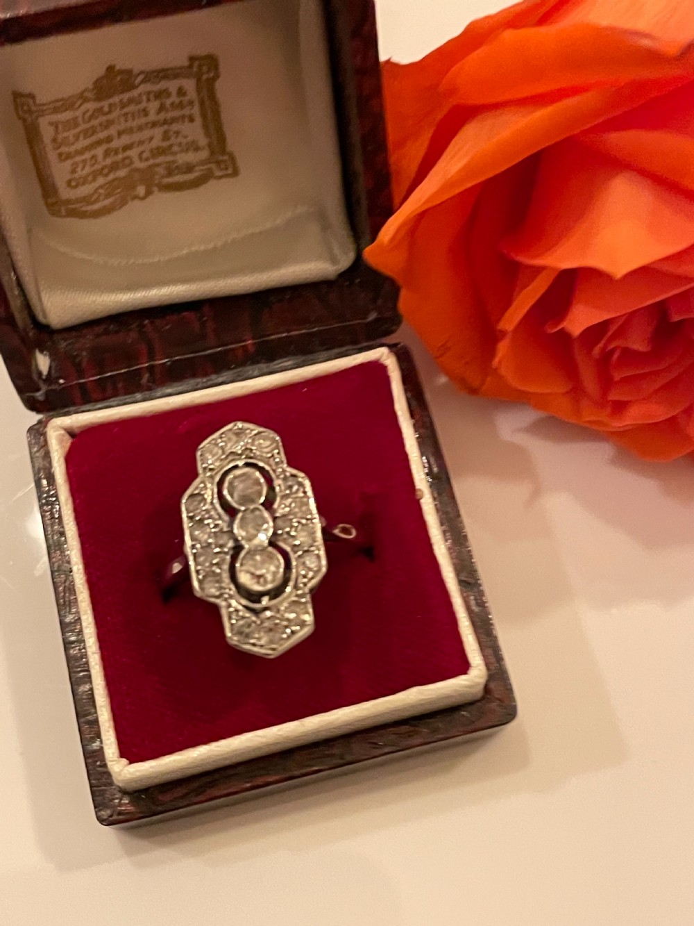 An Edwardian platinum and diamond panel ring featuring three central round diamonds within an elongated geometric frame. View VII
