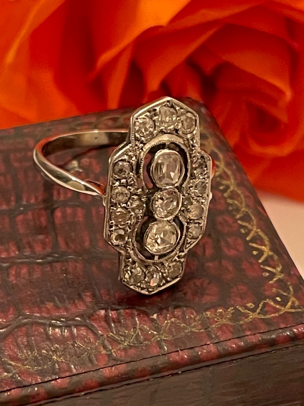 An Edwardian platinum and diamond panel ring featuring three central round diamonds within an elongated geometric frame. View VIII
