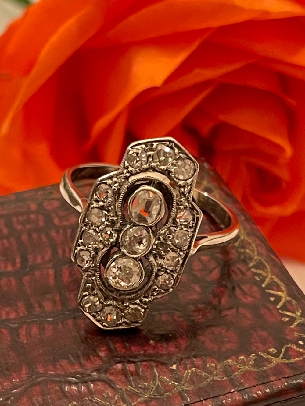 An Edwardian platinum and diamond panel ring featuring three central round diamonds within an elongated geometric frame. View IX