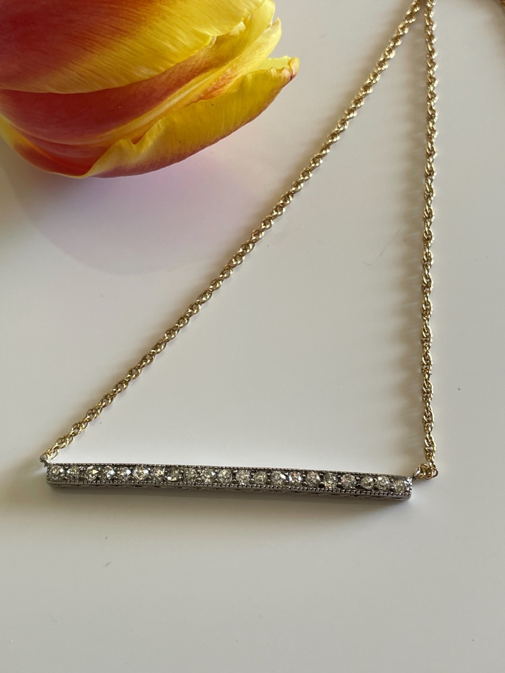 An antique platinum bar set with a row of diamonds suspended from a fine gold chain.