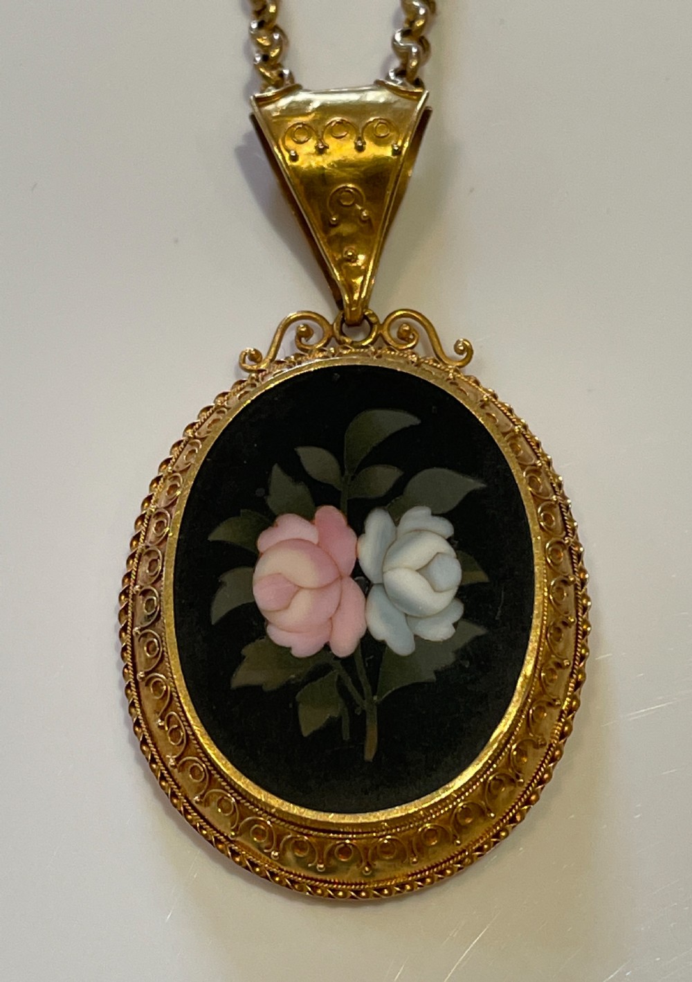 An oval 18ct yellow gold pendant featuring a black Pietra Dura hardstone inlay of pink and white roses suspended from a gold chain. View II
