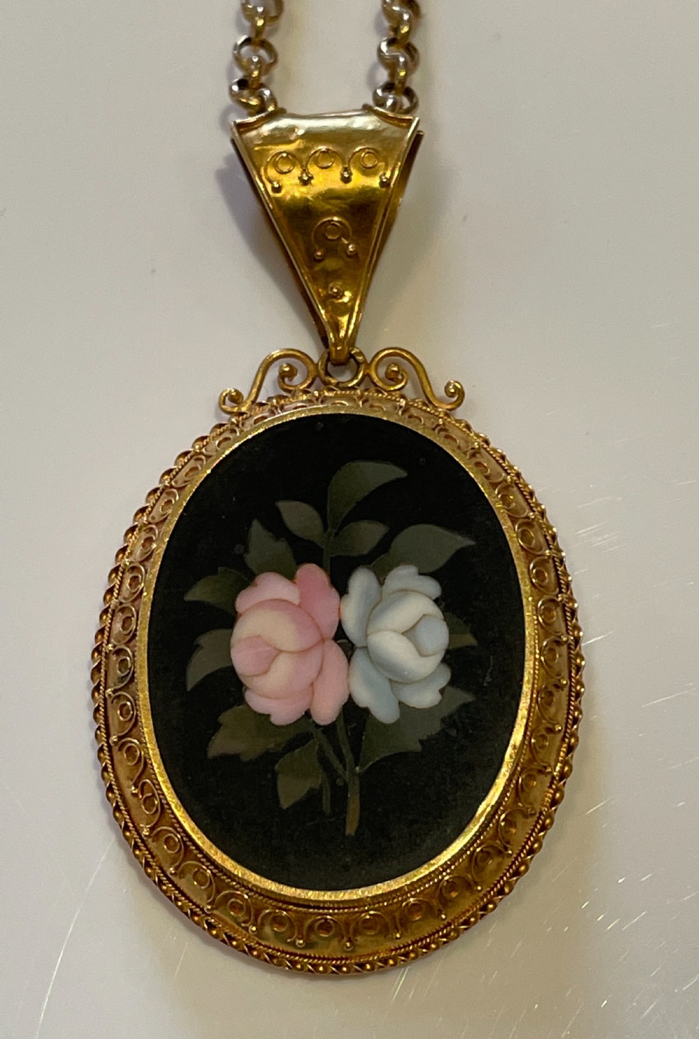 An oval 18ct yellow gold pendant featuring a black Pietra Dura hardstone inlay of pink and white roses suspended from a gold chain. View IV