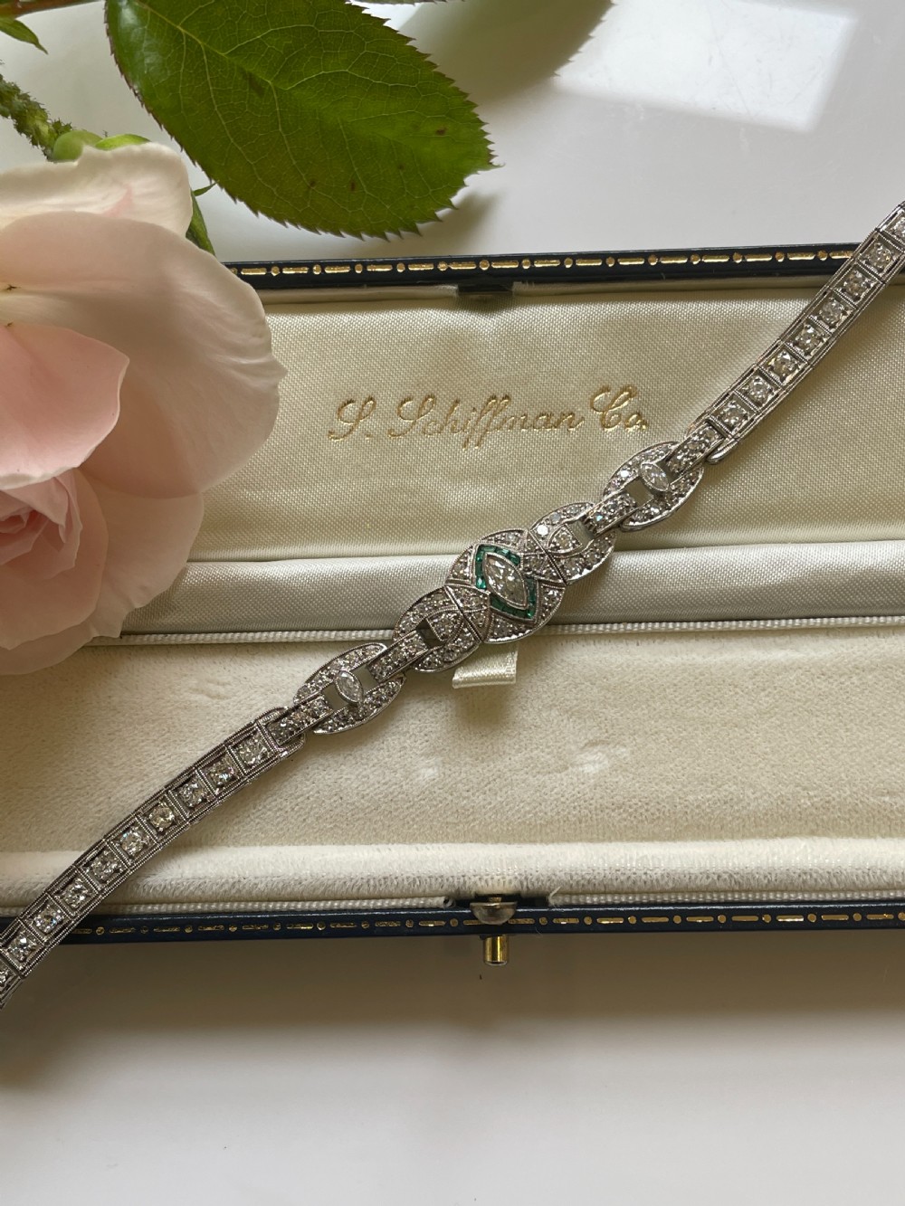 An Art Deco platinum bracelet featuring geometric openwork links set with diamonds and accents of green emeralds around a central marquise diamond.
