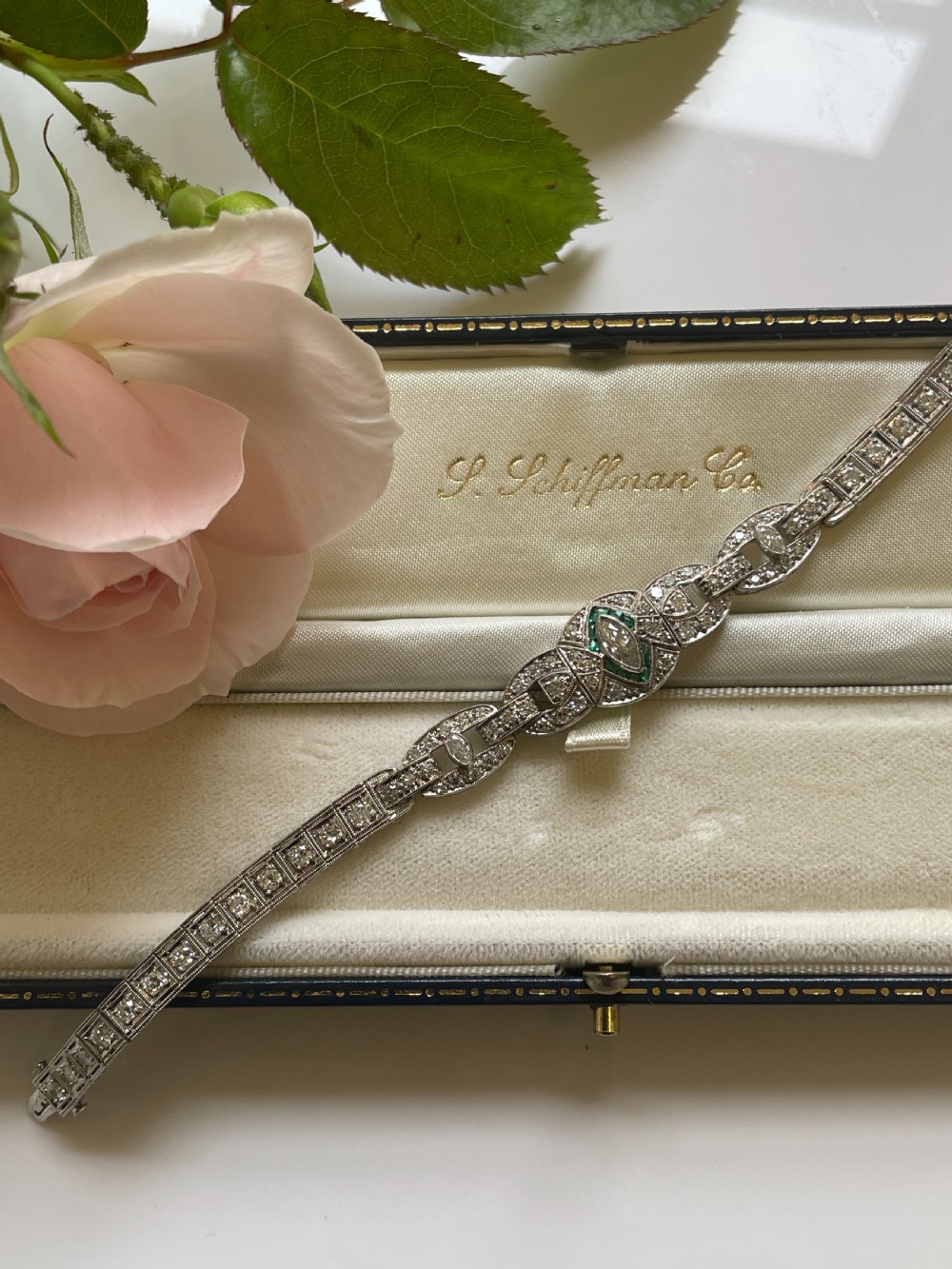 An Art Deco platinum bracelet featuring geometric openwork links set with diamonds and accents of green emeralds around a central marquise diamond. View II
