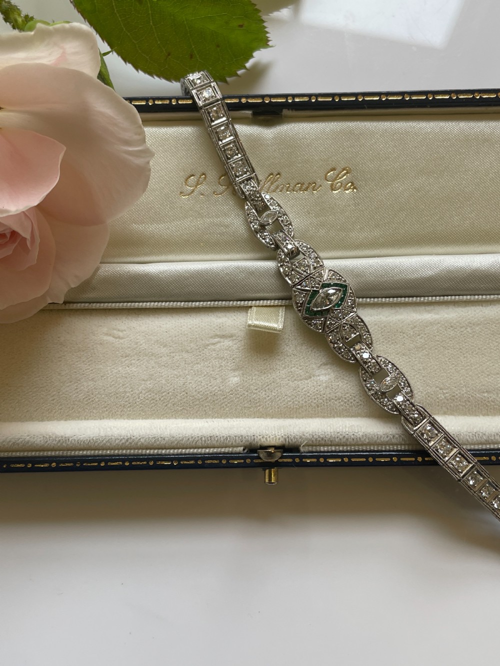 An Art Deco platinum bracelet featuring geometric openwork links set with diamonds and accents of green emeralds around a central marquise diamond. View III