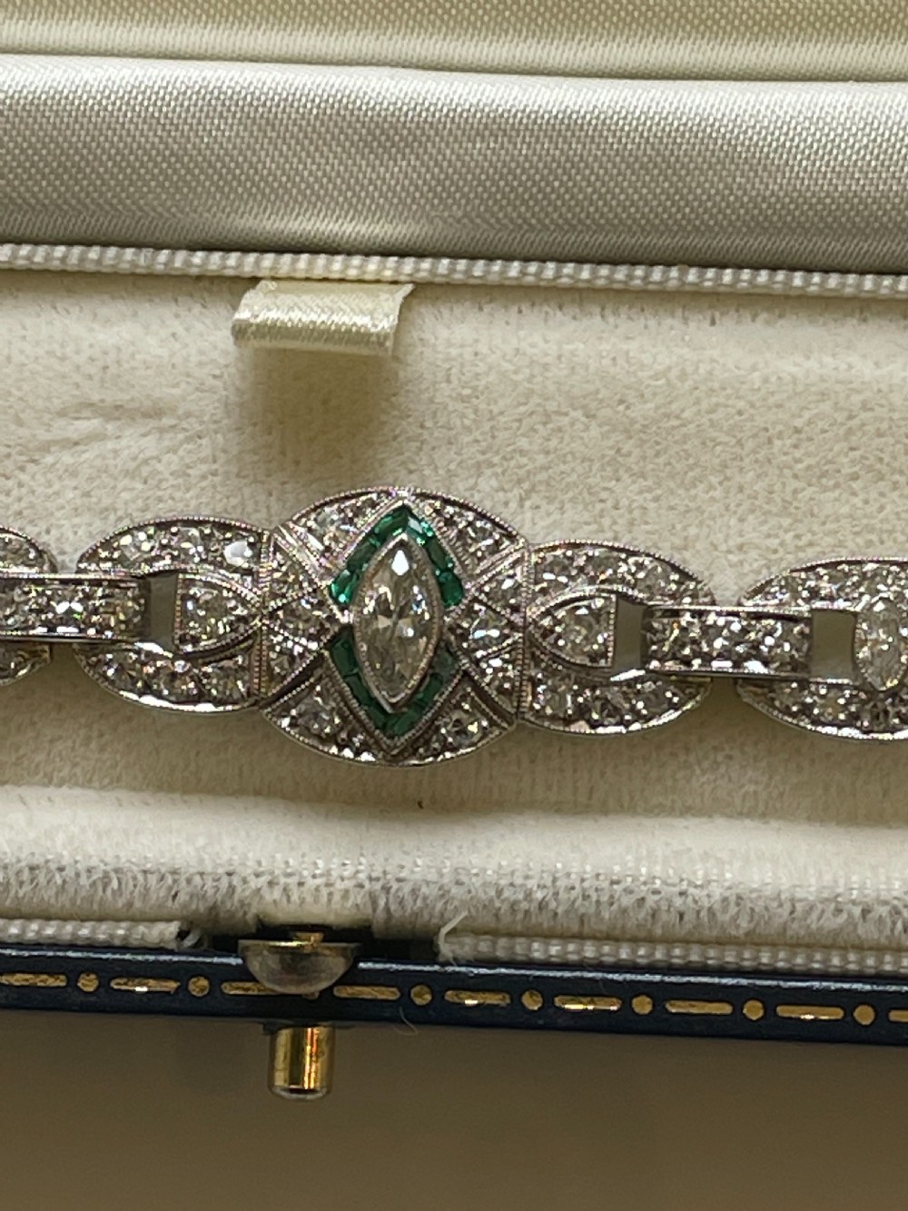 An Art Deco platinum bracelet featuring geometric openwork links set with diamonds and accents of green emeralds around a central marquise diamond. View IV