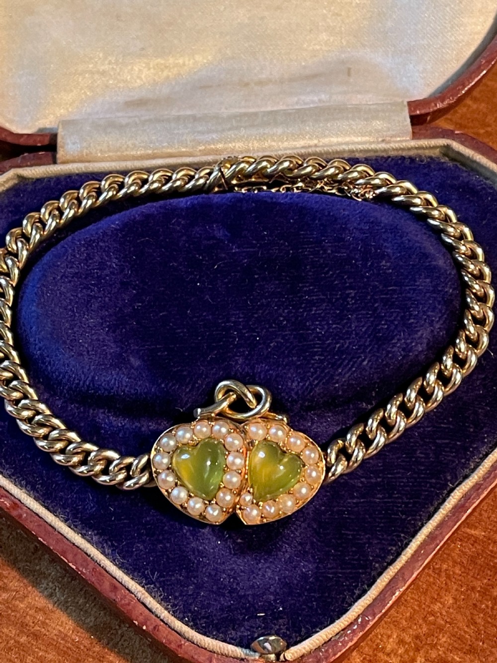 An 18ct yellow gold curb chain bracelet featuring a double heart central motif set with two heart-shaped green chrysoberyl stones framed by small seed pearls.