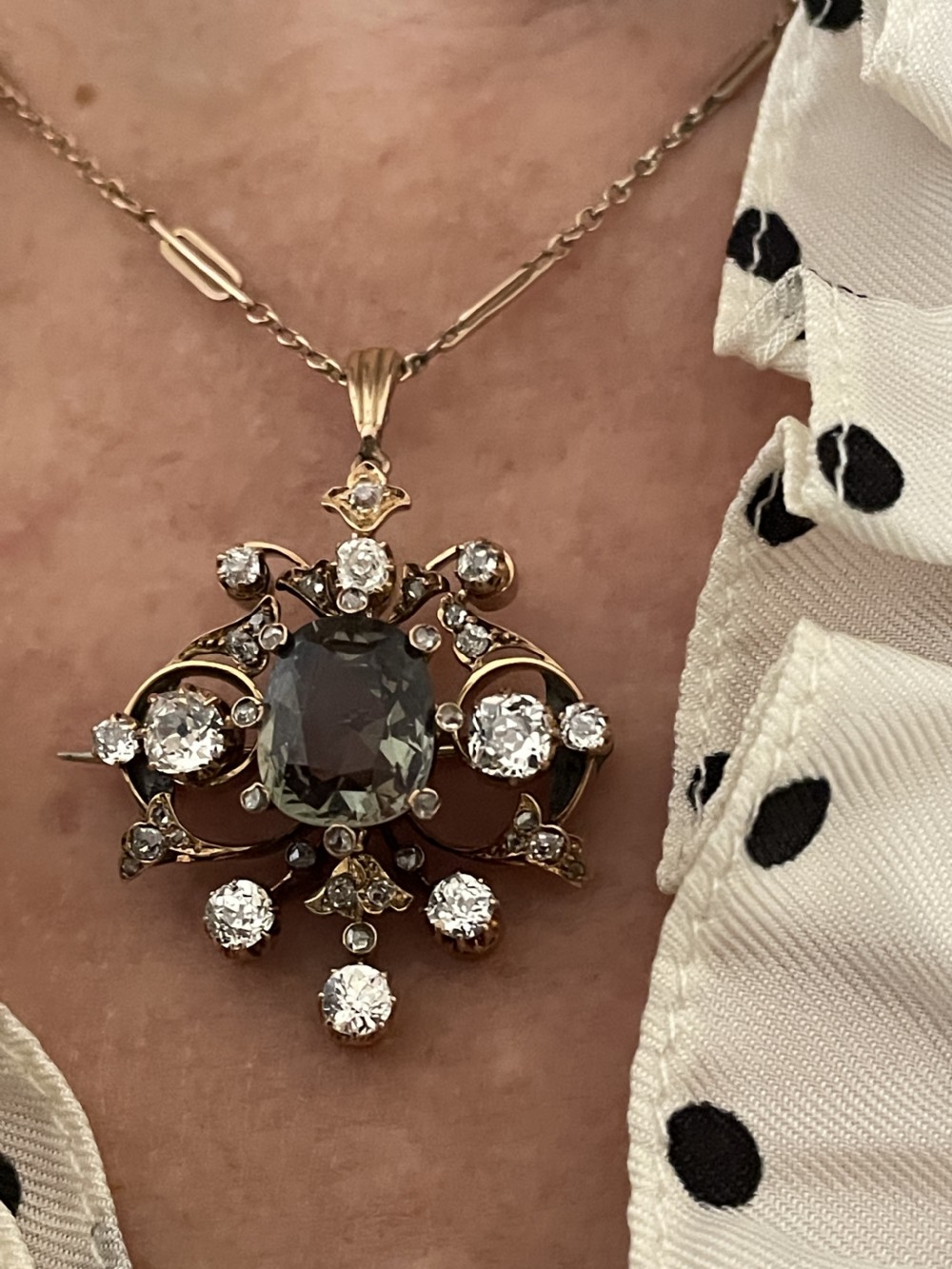 A Victorian gold pendant featuring a central cushion-cut green sapphire within an openwork diamond-set scrollwork frame. View VIII
