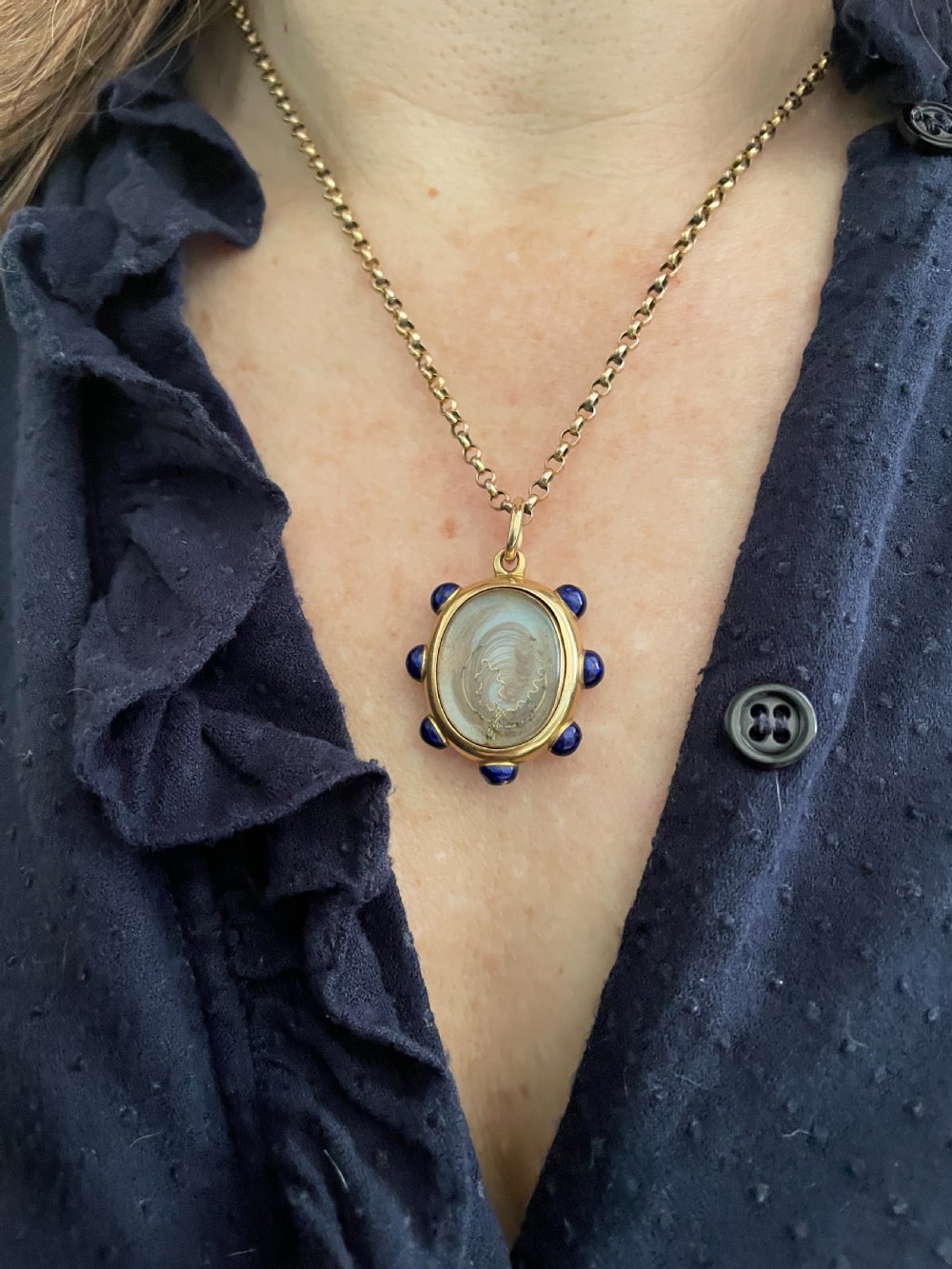 An oval 18ct gold Victorian pendant featuring cobalt blue enamel accents surrounding a glass compartment containing curled human hair work.