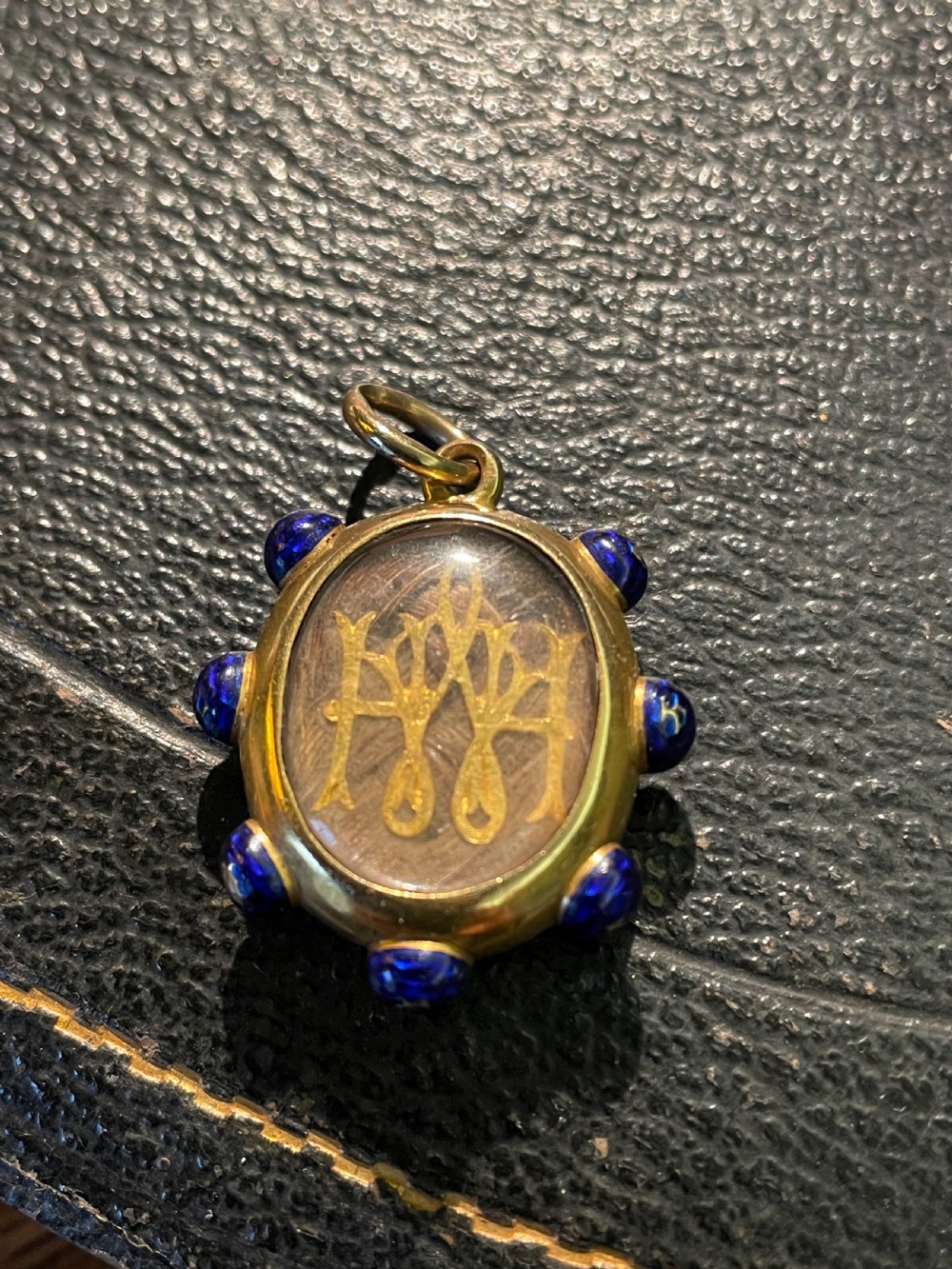 An oval 18ct gold Victorian pendant featuring cobalt blue enamel accents surrounding a glass compartment containing curled human hair work. View II