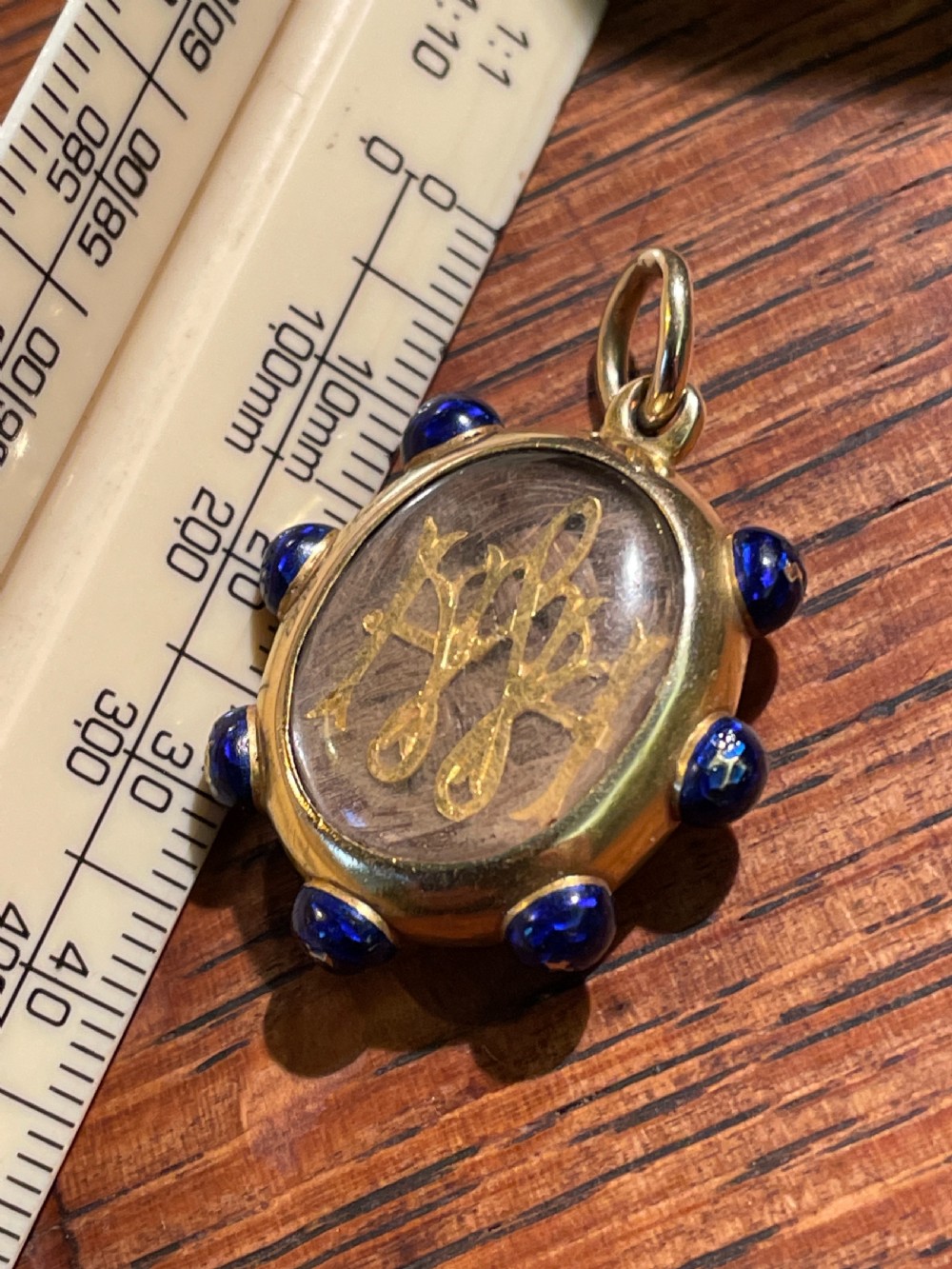An oval 18ct gold Victorian pendant featuring cobalt blue enamel accents surrounding a glass compartment containing curled human hair work. View III