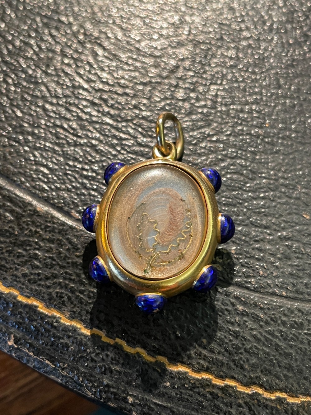 An oval 18ct gold Victorian pendant featuring cobalt blue enamel accents surrounding a glass compartment containing curled human hair work. View IV