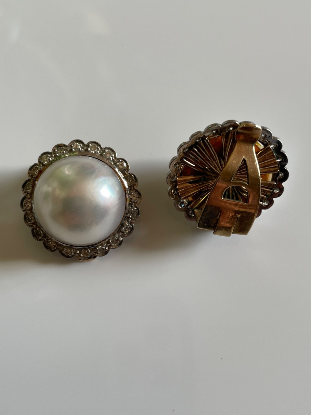 A pair of large circular mid-century earrings featuring central round pearls encircled by scalloped metal halos set with small diamonds. View III