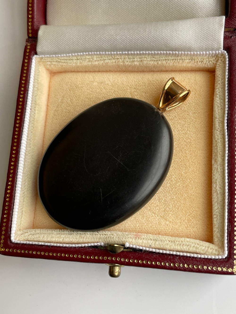 An oval black marble pendant with a floral pietra dura stone inlay and a polished gold bail. View II