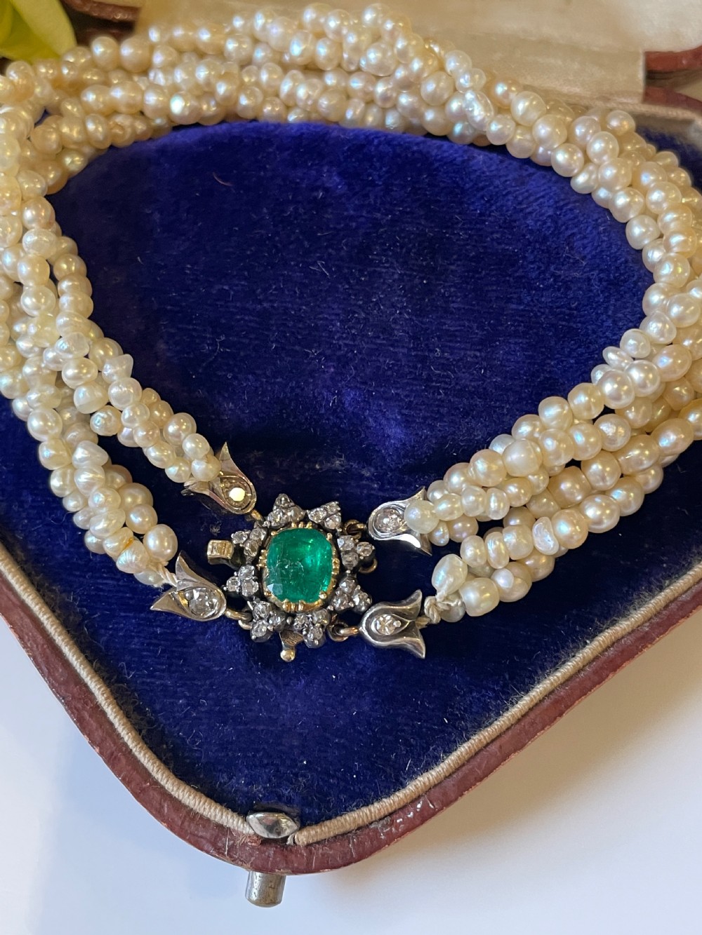 A multi-strand natural white pearl bracelet featuring an oval green emerald centre surrounded by a cluster of diamonds with leaf-shaped caps.