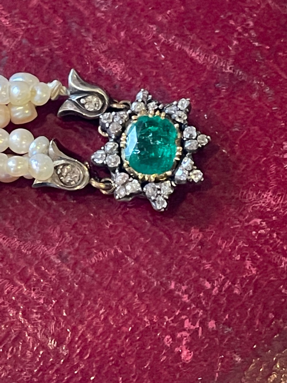 A multi-strand natural white pearl bracelet featuring an oval green emerald centre surrounded by a cluster of diamonds with leaf-shaped caps. View II