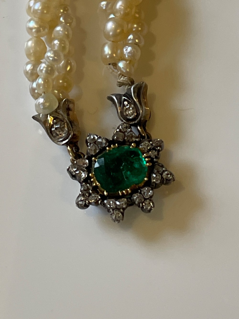 A multi-strand natural white pearl bracelet featuring an oval green emerald centre surrounded by a cluster of diamonds with leaf-shaped caps. View III