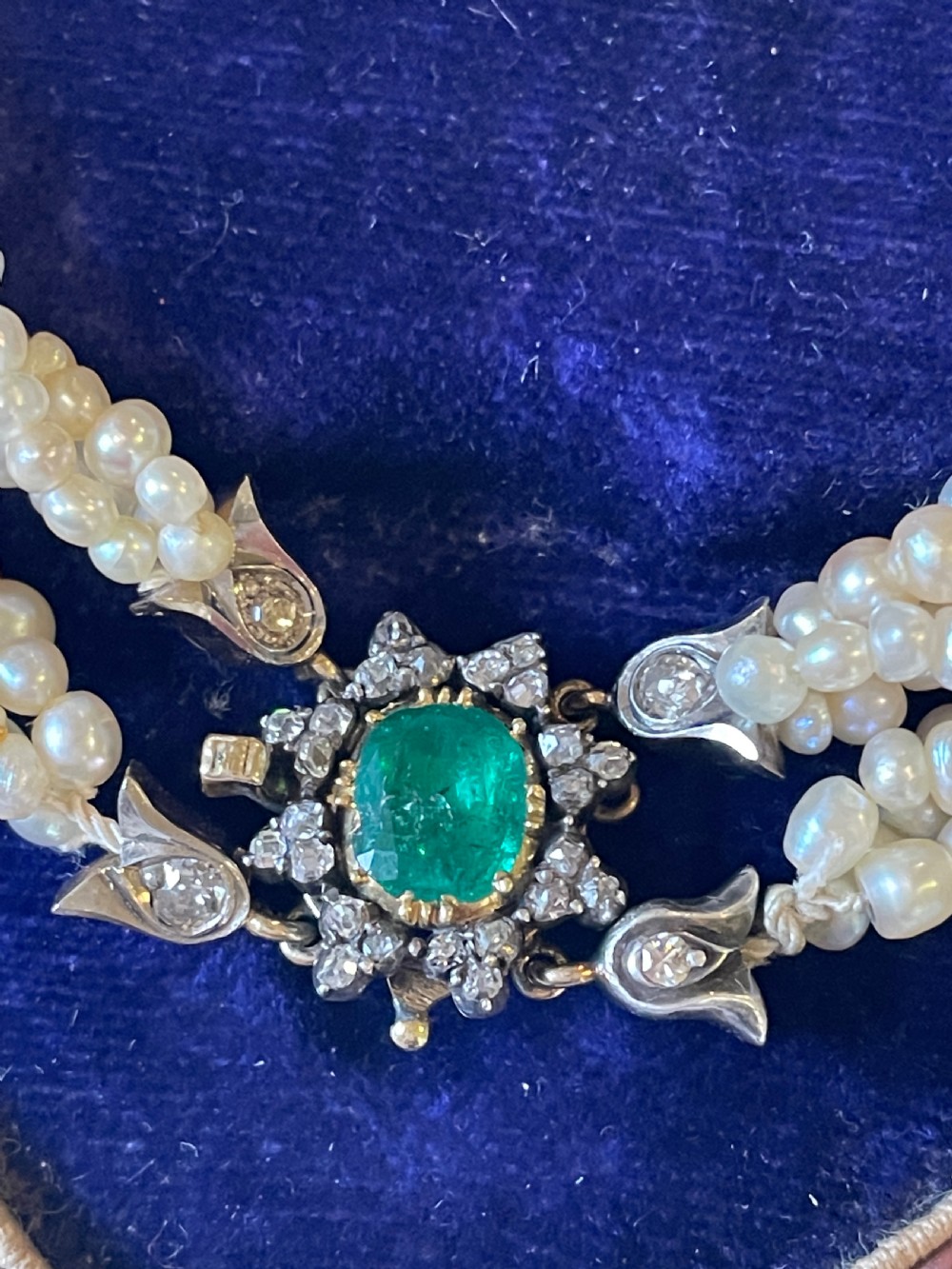 A multi-strand natural white pearl bracelet featuring an oval green emerald centre surrounded by a cluster of diamonds with leaf-shaped caps. View V