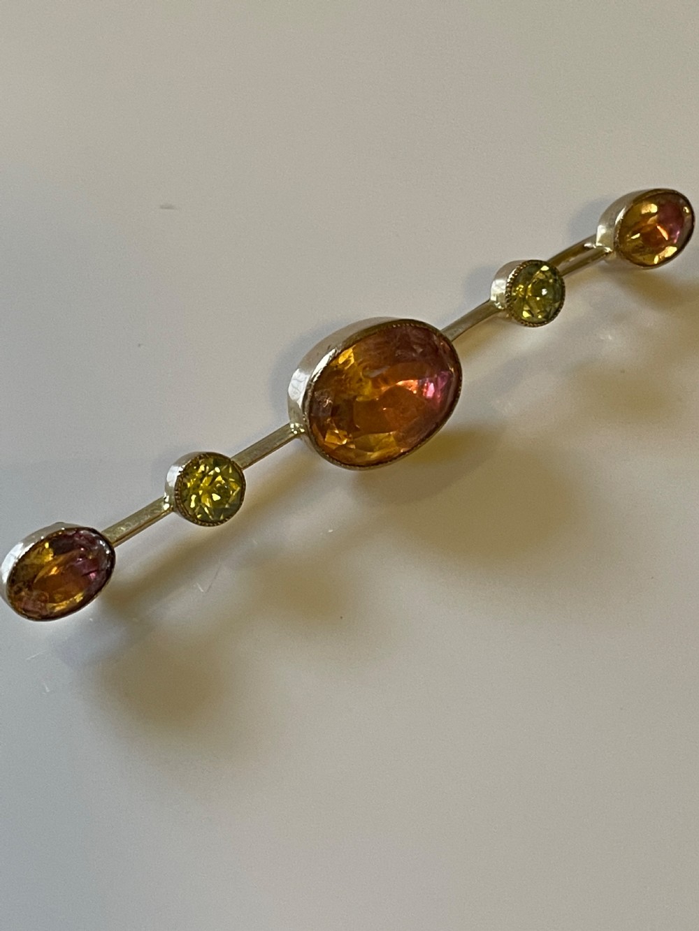 An antique gold bar brooch set with a central oval pink topaz, flanked by two round pale chrysoberyls and two smaller oval pink topazes in rub-over settings. View II