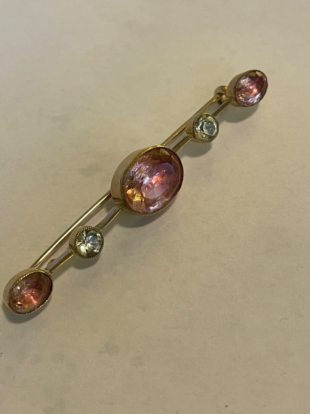 An antique gold bar brooch set with a central oval pink topaz, flanked by two round pale chrysoberyls and two smaller oval pink topazes in rub-over settings. View III