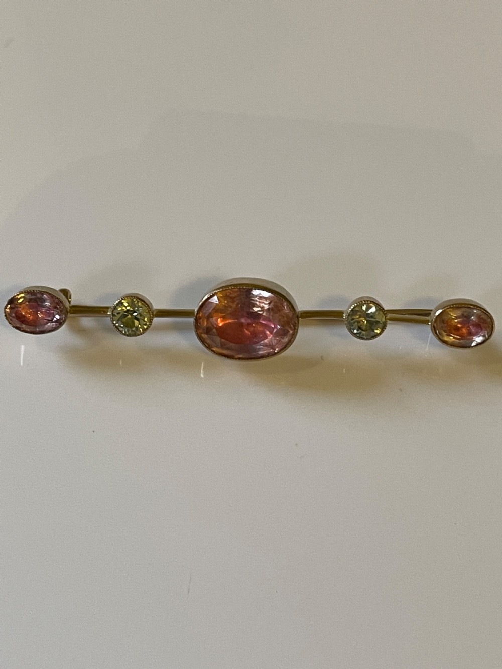 An antique gold bar brooch set with a central oval pink topaz, flanked by two round pale chrysoberyls and two smaller oval pink topazes in rub-over settings. View IV