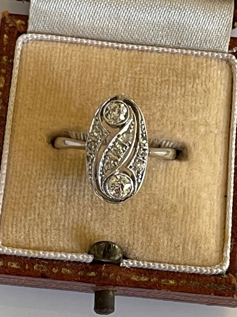 An Edwardian silver-toned ring featuring an oval panel with two prominent diamonds surrounded by swirl filigree and smaller accent diamonds. View II
