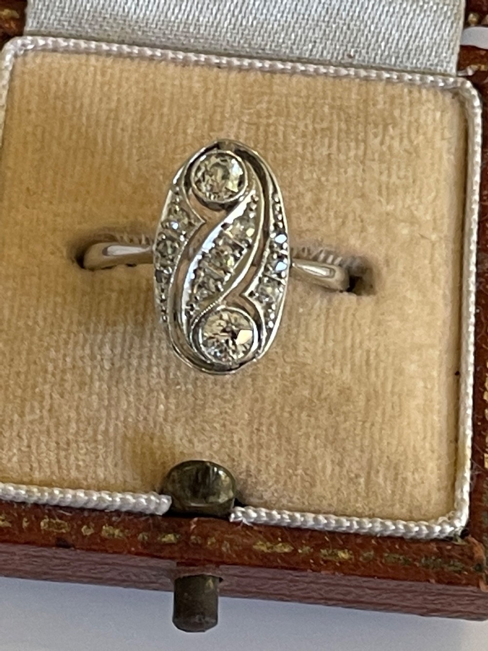 An Edwardian silver-toned ring featuring an oval panel with two prominent diamonds surrounded by swirl filigree and smaller accent diamonds. View III