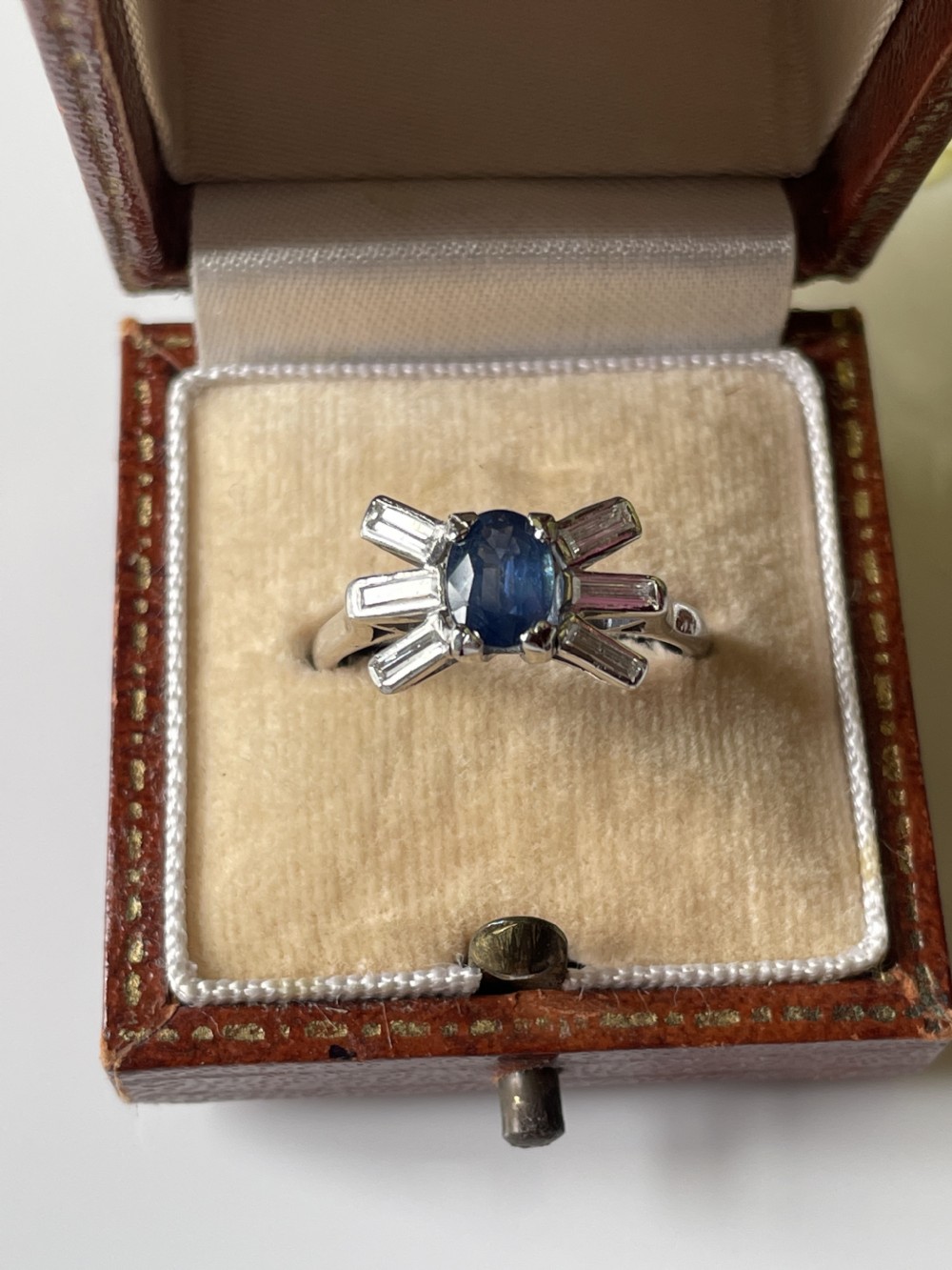 An Art Deco platinum ring featuring a central oval blue sapphire flanked by fanned baguette-cut diamonds. View II