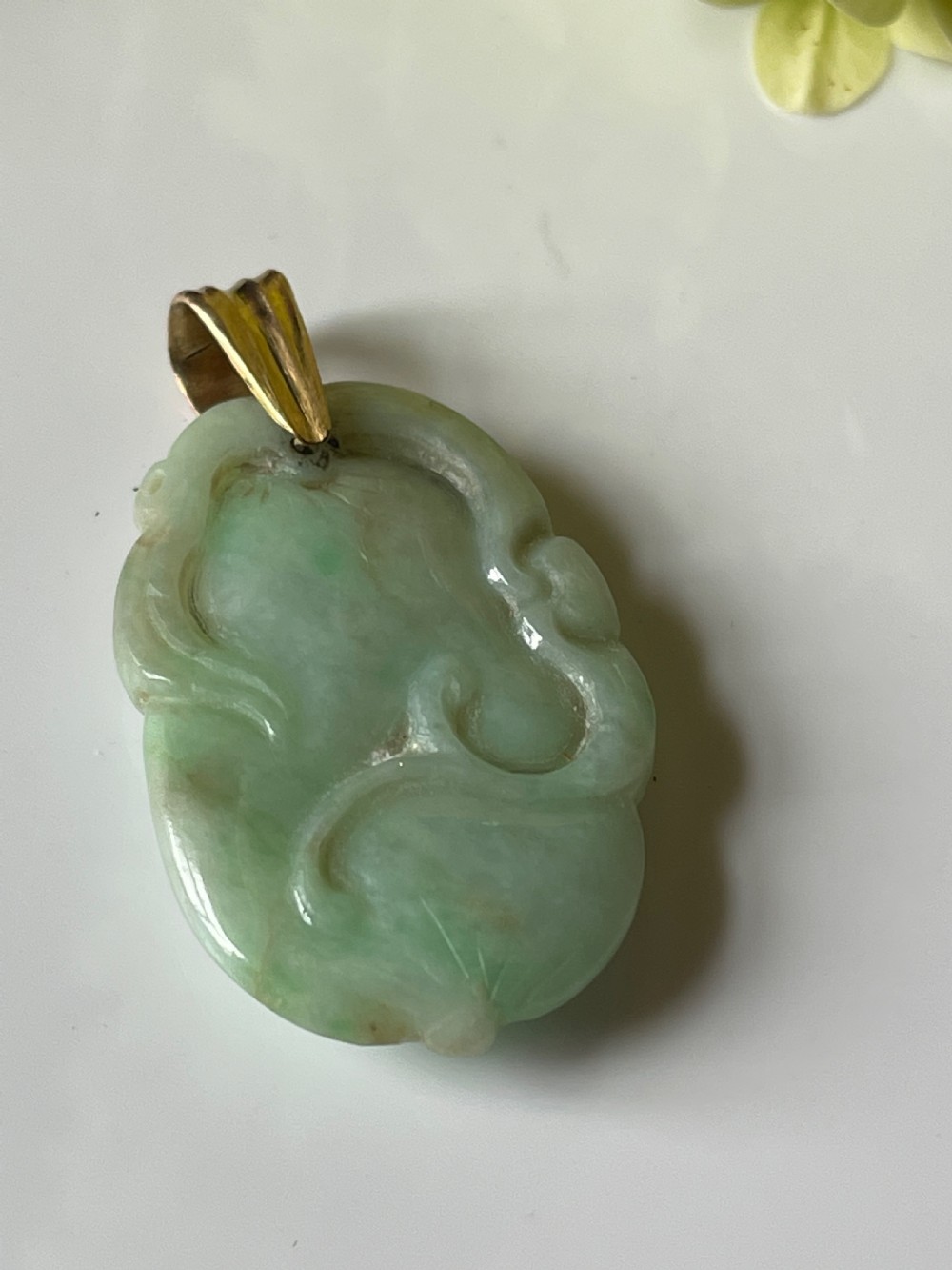 A carved pale green jadeite pendant featuring stylised botanical motifs suspended from a gold bale.
