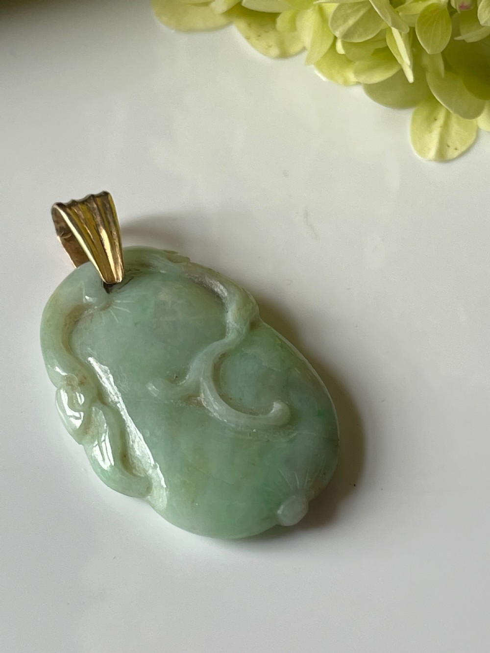 A carved pale green jadeite pendant featuring stylised botanical motifs suspended from a gold bale. View II