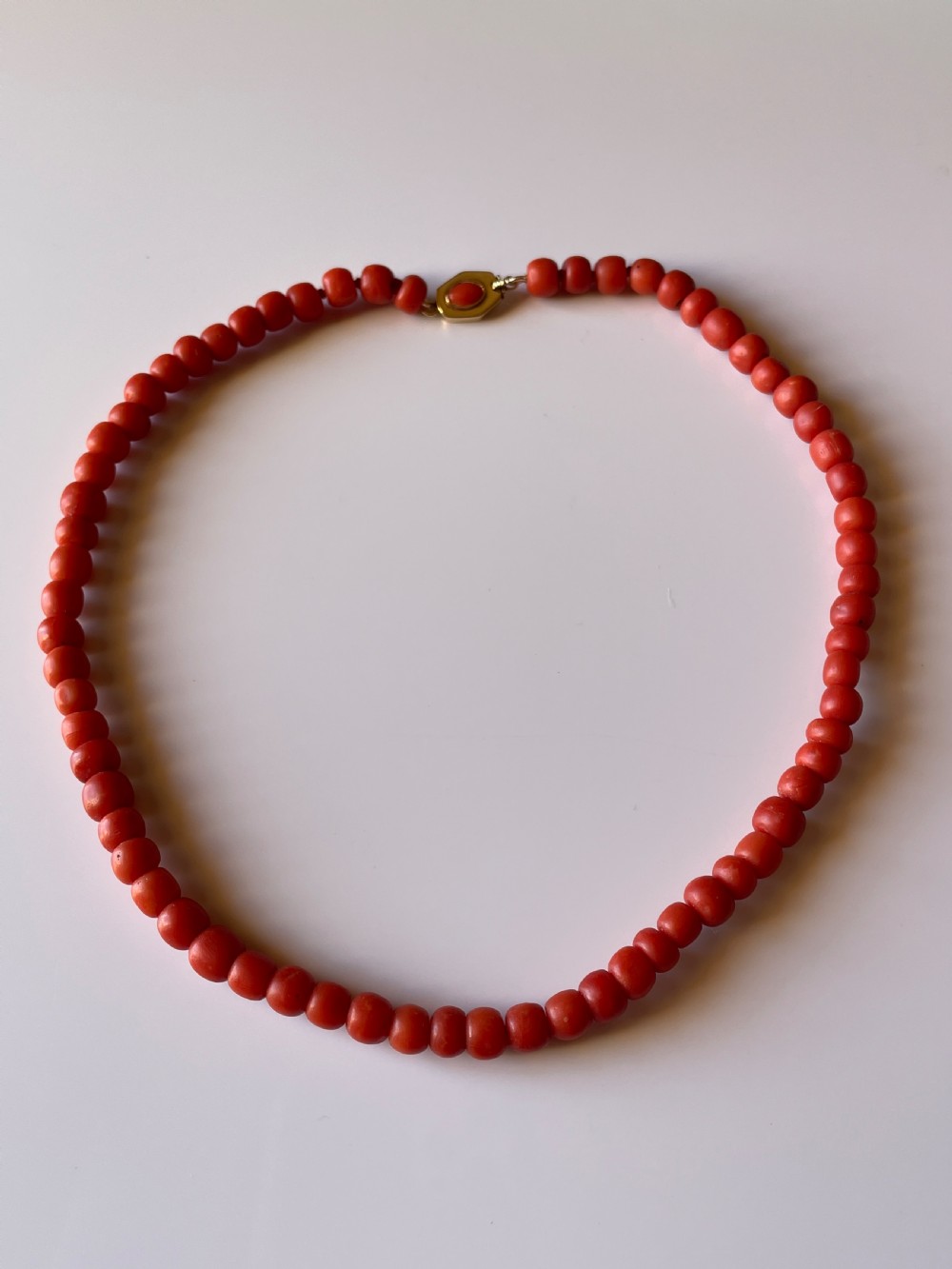 A hand holding a single strand of natural un-dyed red coral beads featuring a gold push clasp. View II