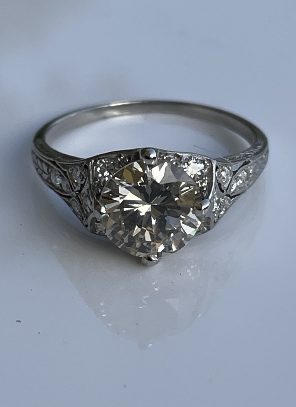 An Art Deco platinum ring featuring a large central round diamond with smaller accent diamonds and leaf motifs engraved into the shoulders. View IV