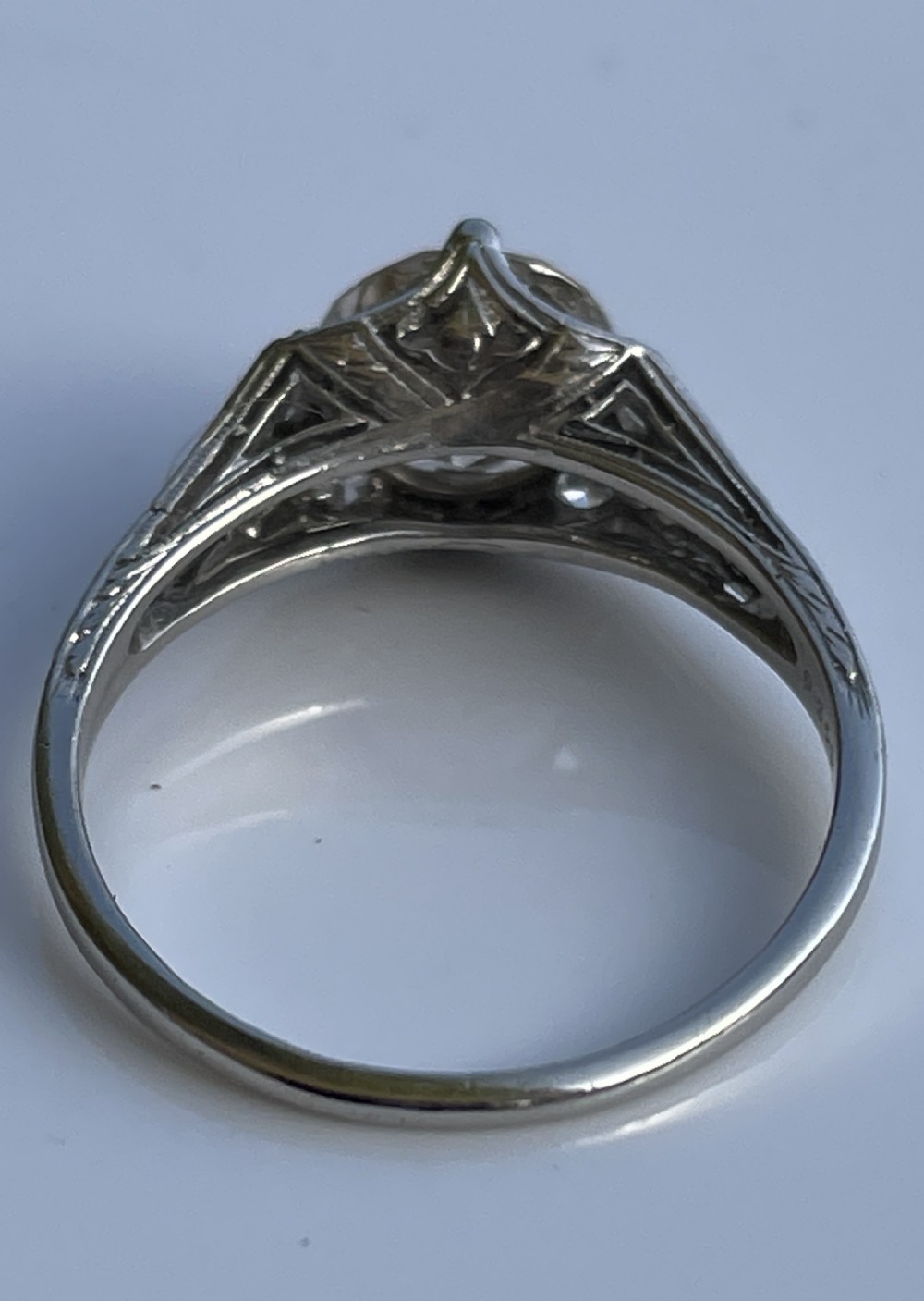 An Art Deco platinum ring featuring a large central round diamond with smaller accent diamonds and leaf motifs engraved into the shoulders. View V