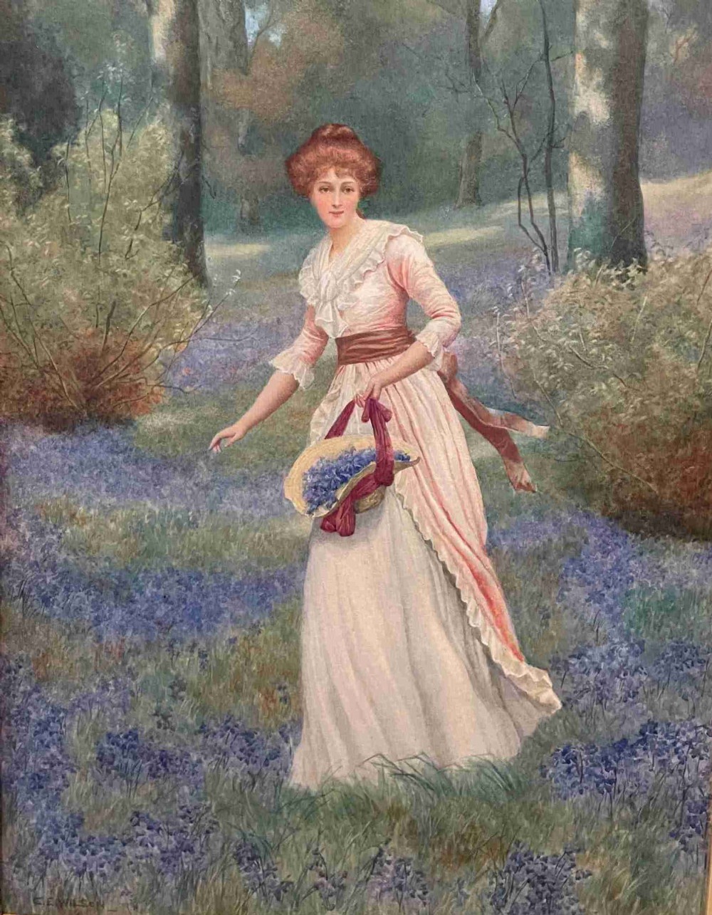 An Edwardian watercolour painting depicting a woman in a pink dress and brown sash walking through a bluebell woodland while holding a basket.