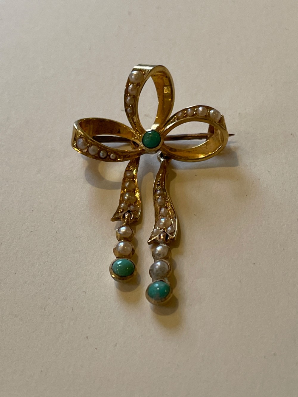An Edwardian gold bow brooch embellished with seed pearls along the ribbon loops and turquoise cabochons at the central knot and tail ends. View II
