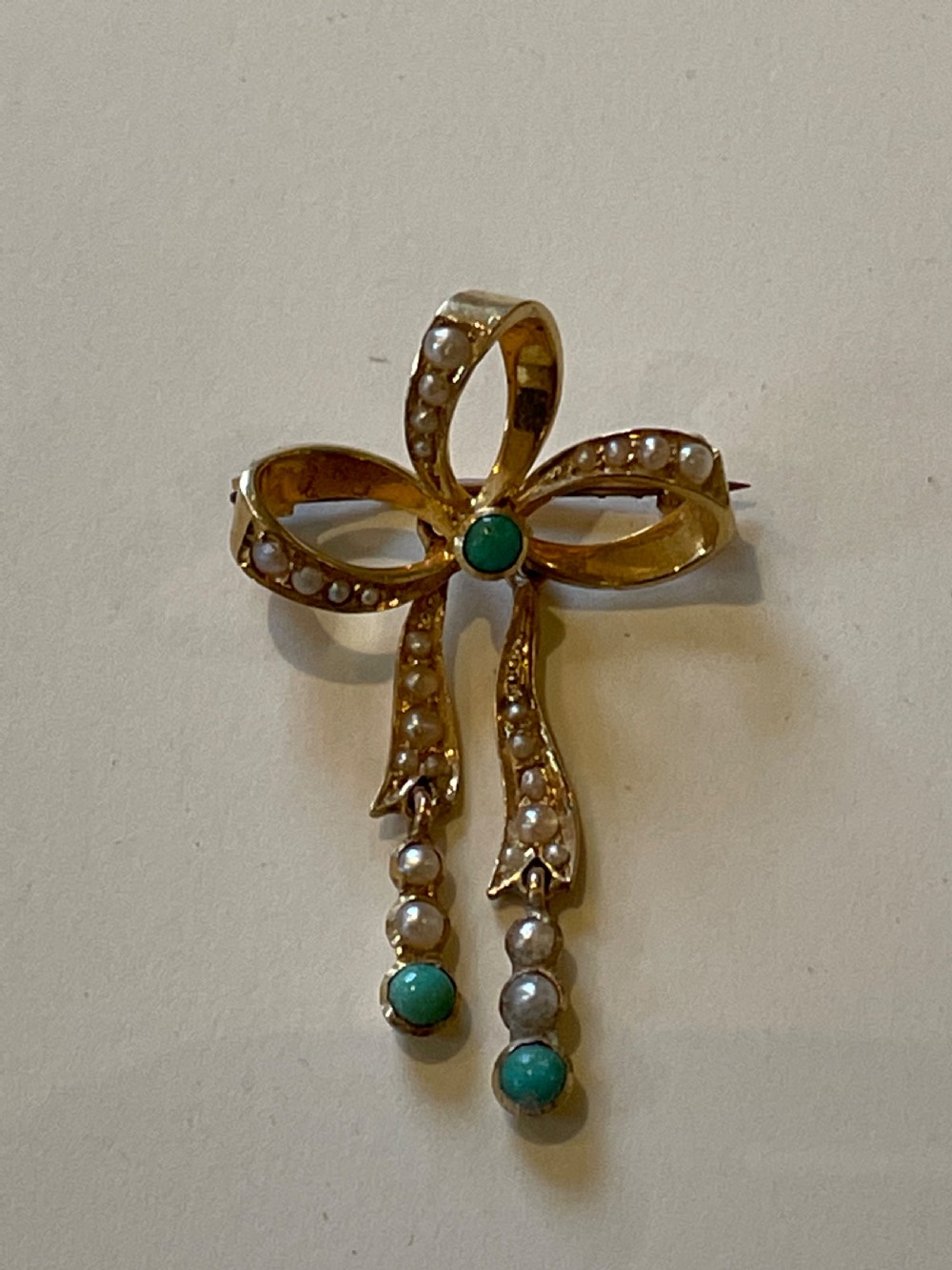 An Edwardian gold bow brooch embellished with seed pearls along the ribbon loops and turquoise cabochons at the central knot and tail ends. View III
