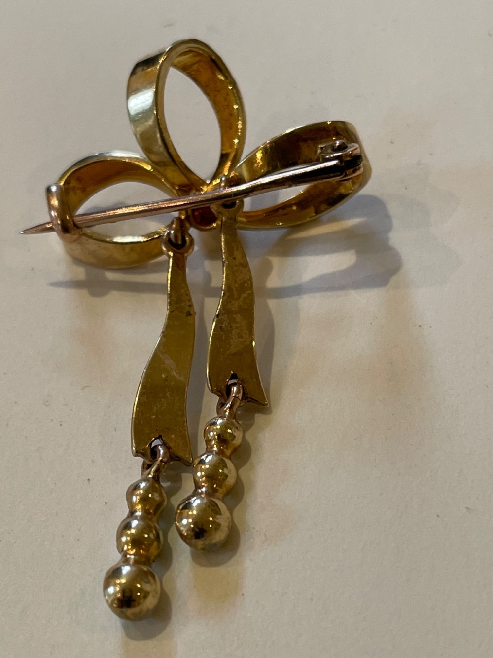 An Edwardian gold bow brooch embellished with seed pearls along the ribbon loops and turquoise cabochons at the central knot and tail ends. View IV