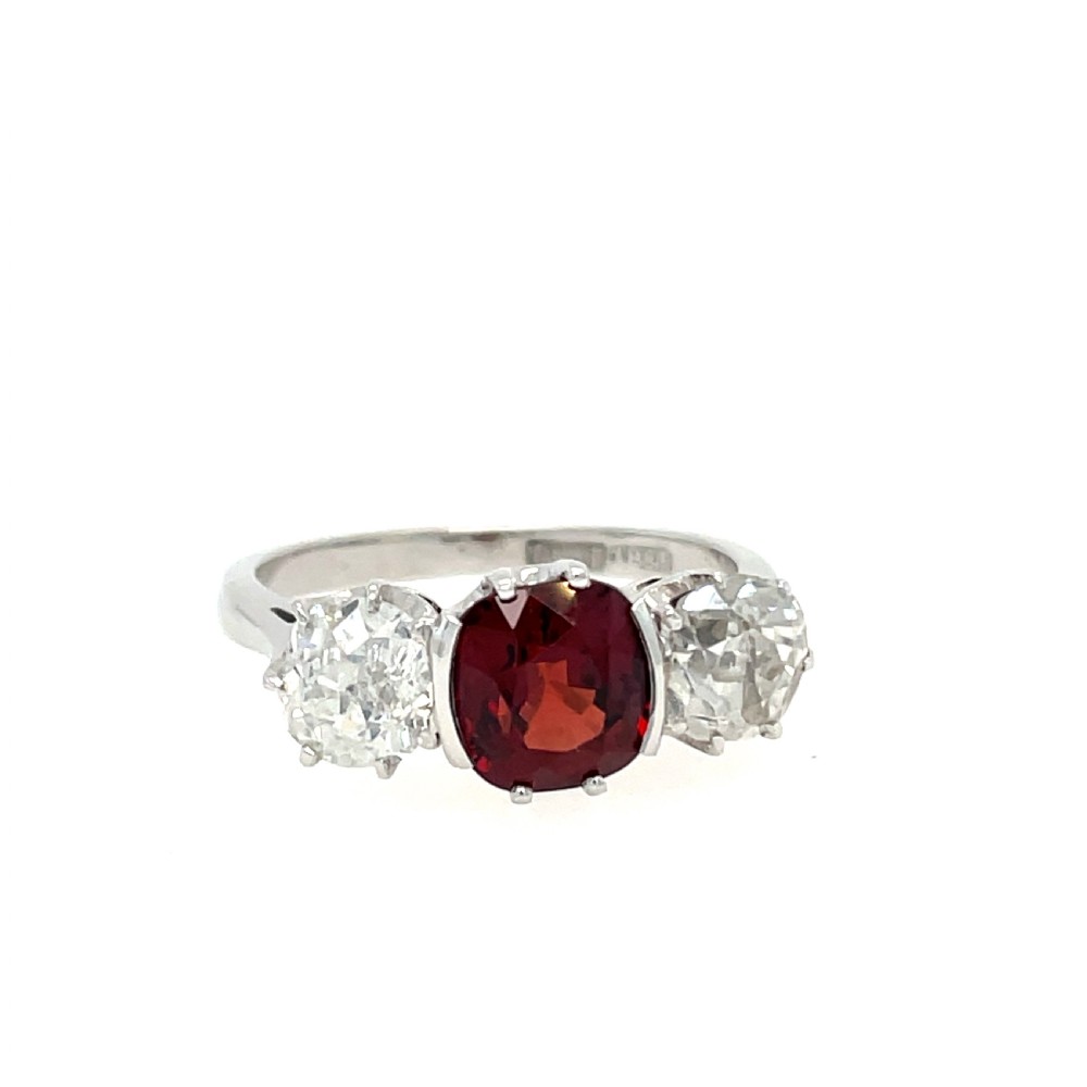 An antique platinum three-stone ring featuring a central cushion-cut red spinel flanked by two old cut diamonds.