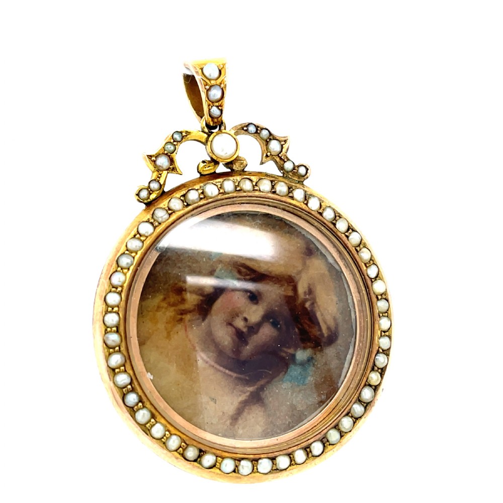 A circular Edwardian 9ct gold photograph locket framed with seed pearls, enclosing a miniature portrait under glass.