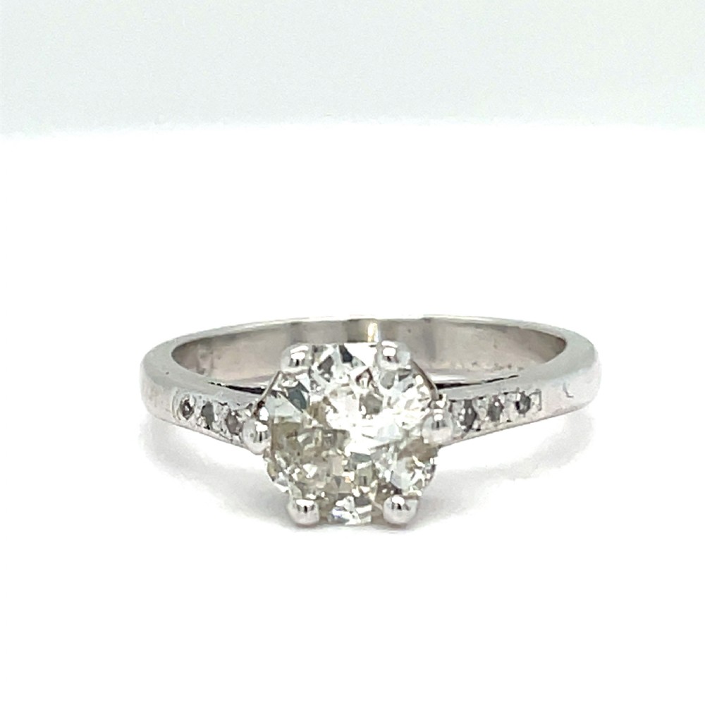 An Art Deco style 18ct white gold engagement ring featuring a central round diamond solitaire in a multi-claw setting with accent diamonds set into the shoulders.