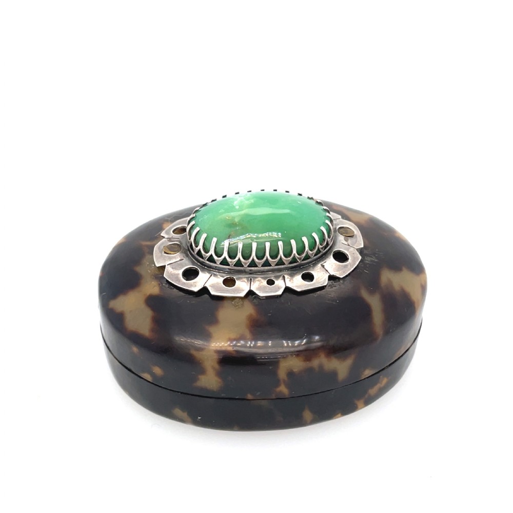 An oval dark brown tortoiseshell box featuring a polished green oval jadeite cabochon set in a silver mount on the lid.