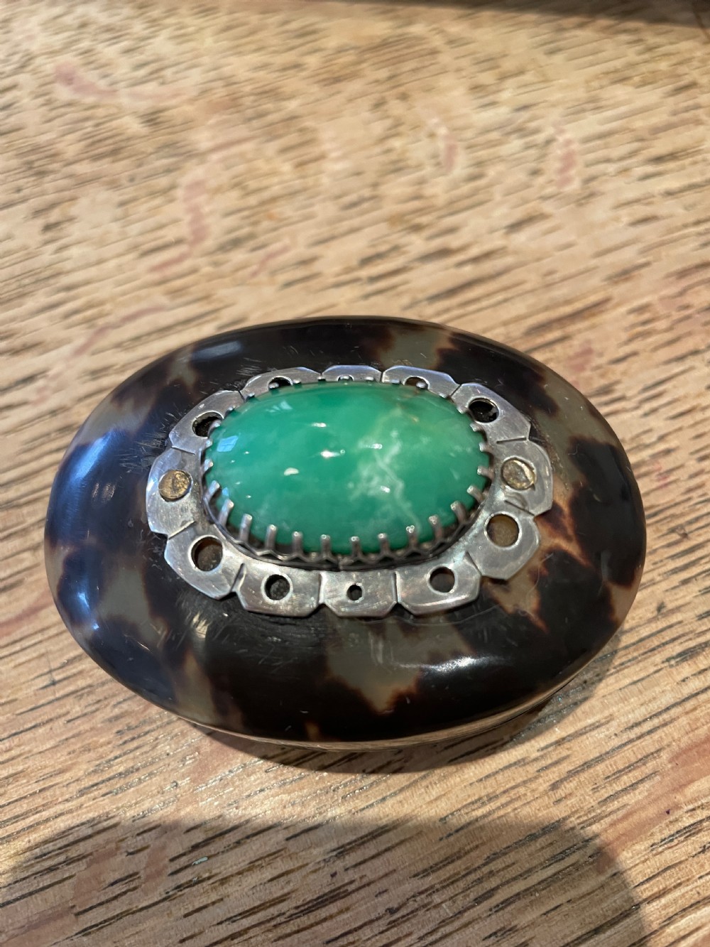 An oval dark brown tortoiseshell box featuring a polished green oval jadeite cabochon set in a silver mount on the lid. View III