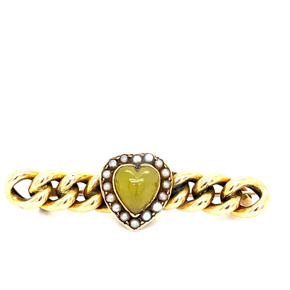 A Victorian 15ct gold bar brooch crafted with a curb link design and a central heart-shaped green agate cabochon surrounded by seed pearls.