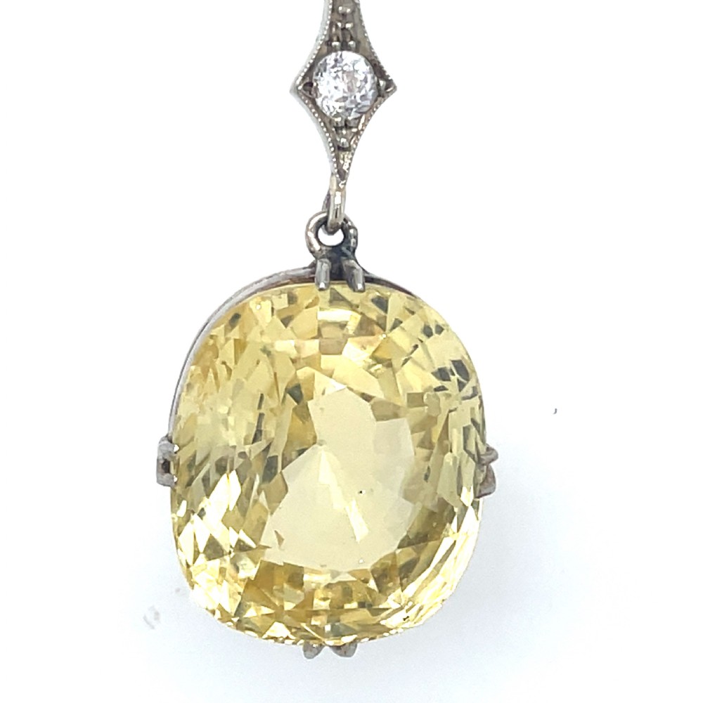 An Edwardian platinum pendant featuring an oval cushion-cut yellow sapphire suspended from a diamond-set drop chain. View II