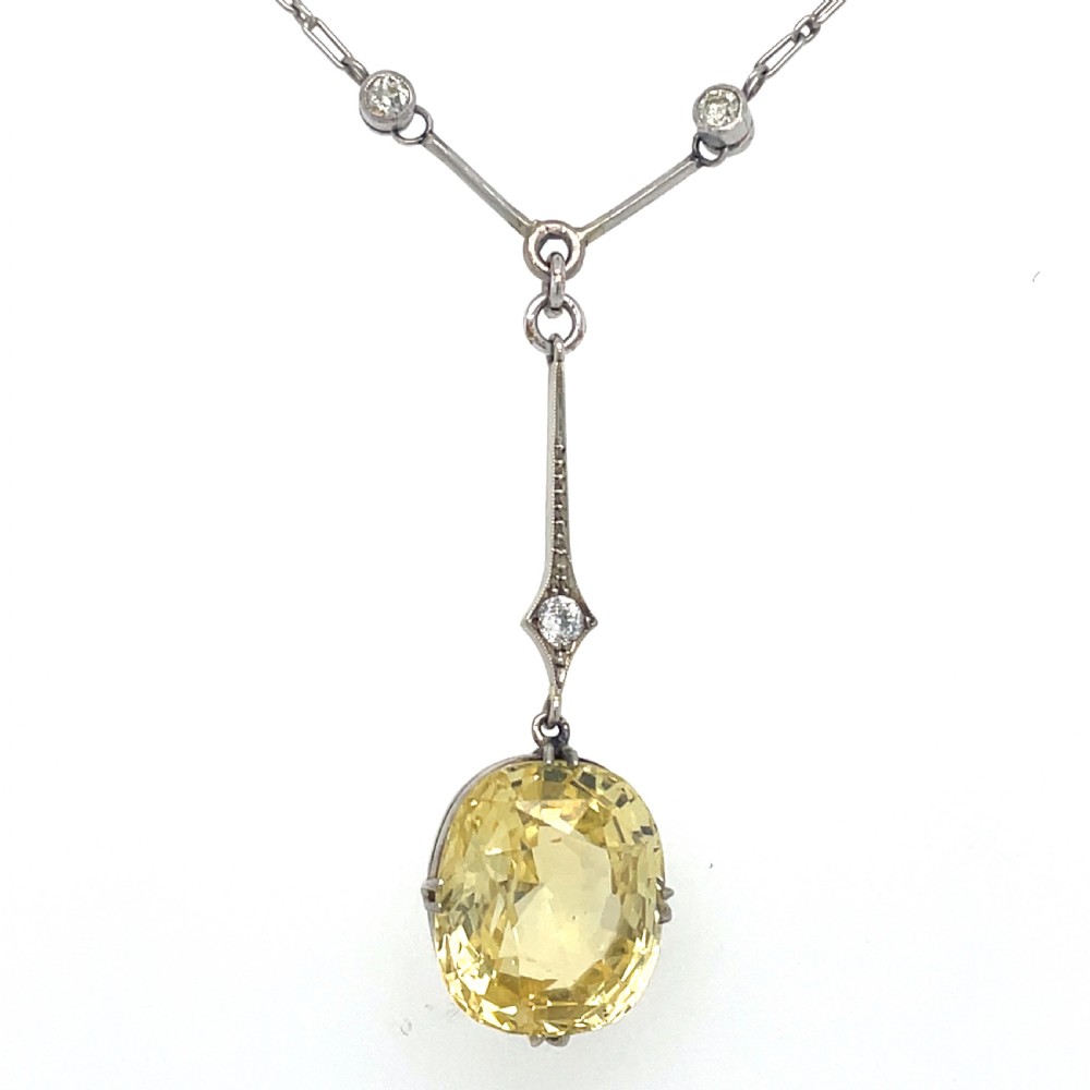 An Edwardian platinum pendant featuring an oval cushion-cut yellow sapphire suspended from a diamond-set drop chain. View IV