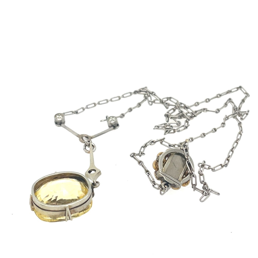 An Edwardian platinum pendant featuring an oval cushion-cut yellow sapphire suspended from a diamond-set drop chain. View VI